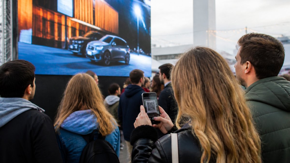 Bezoekers bij een groot LED-scherm op een evenement, een van hen scant een QR-code met de smartphone terwijl anderen naar het scherm kijken
