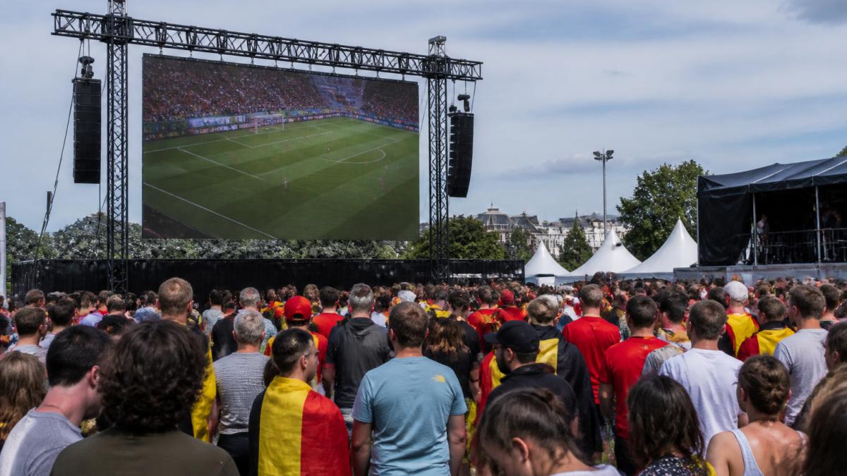 Groot LED-scherm opgesteld op buitenevenement met publiek dat naar het scherm kijkt, waarbij de beeldkwaliteit en zichtbaarheid overdag duidelijk zijn