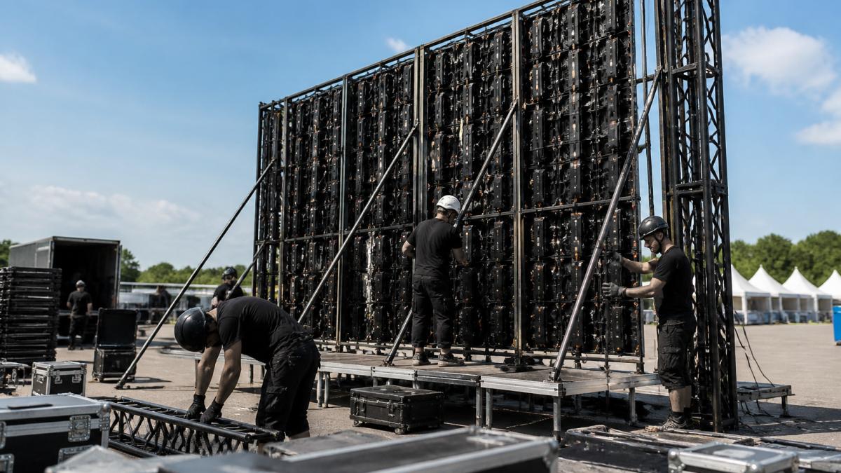 Professioneel team van technici bouwt een groot LED-scherm op op een buitenevenement, met veiligheidshelmen, werkhandschoenen en gereedschap zichtbaar, onder helder daglicht